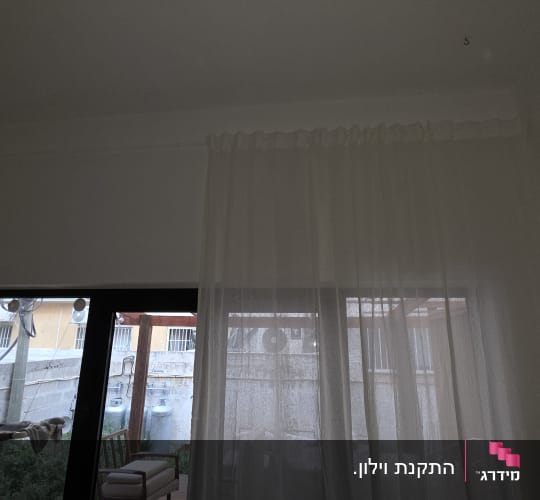 וילון לבן מותקן מעל ויטרינת זכוכית בבית